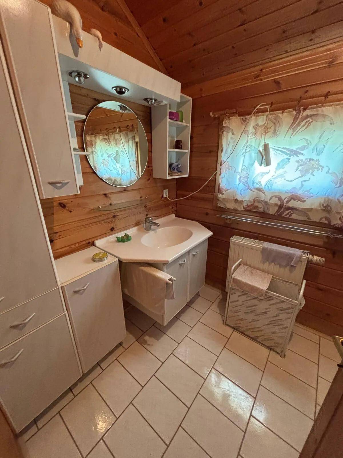 Badezimmer mit Holzvertäfelung, Waschbecken, Spiegel und Heizkörper, ausgestattet mit Fliesenboden.
