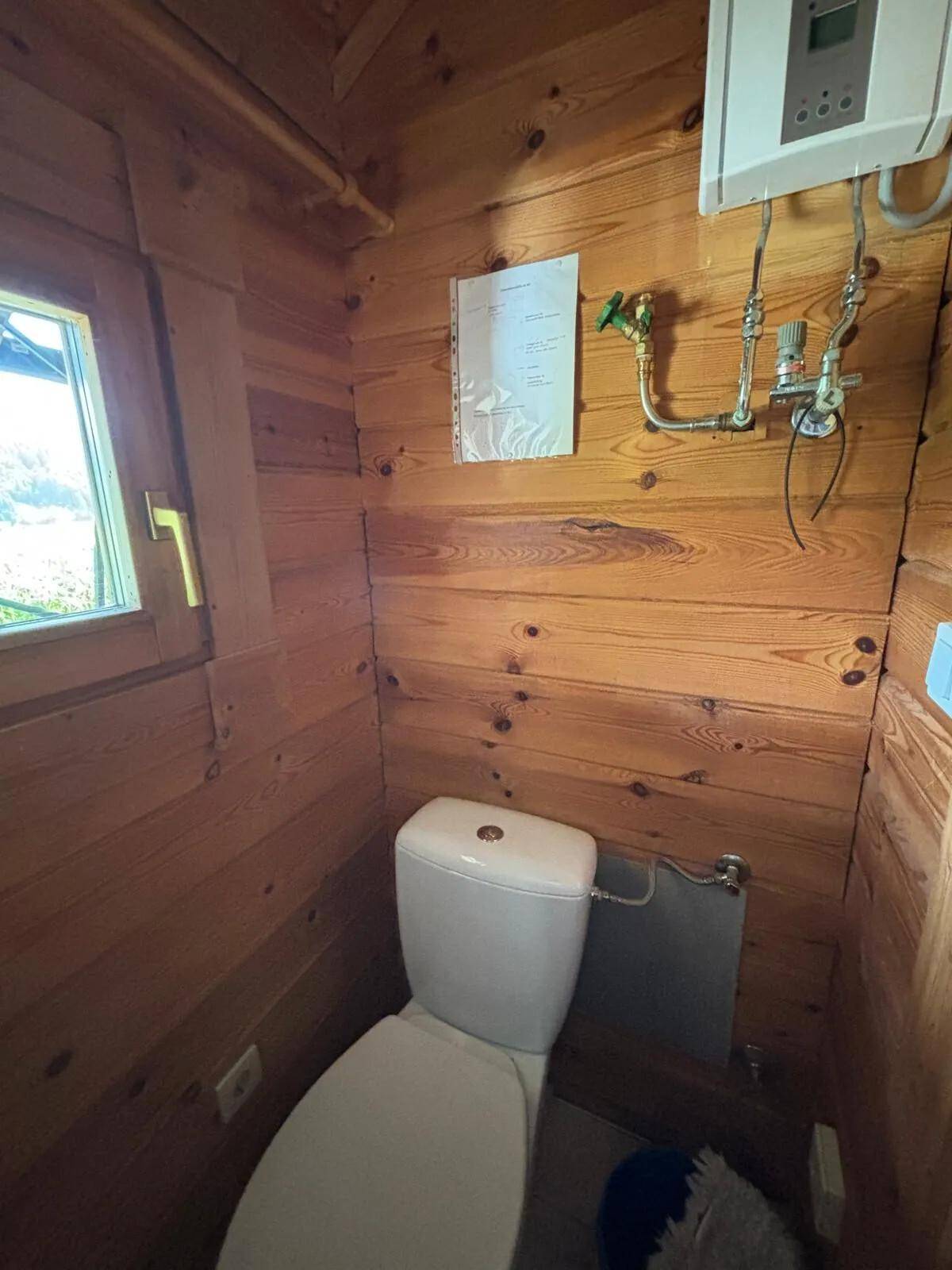 Kleines WC mit Holzvertäfelung und Fenster, einfach und funktional eingerichtet.