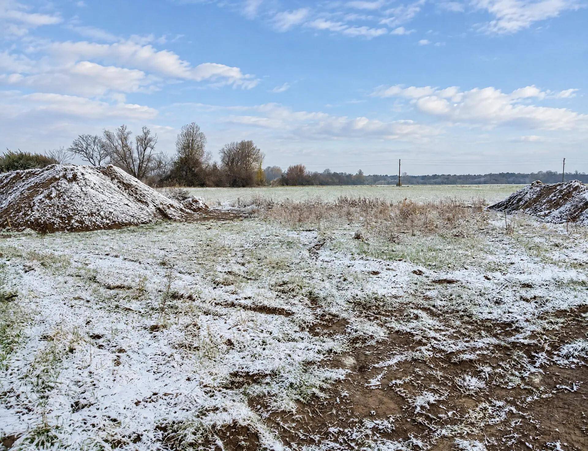 Schneebedecktes Grundstück mit Erdhügeln und winterlicher Landschaft unter bewölktem Himmel.