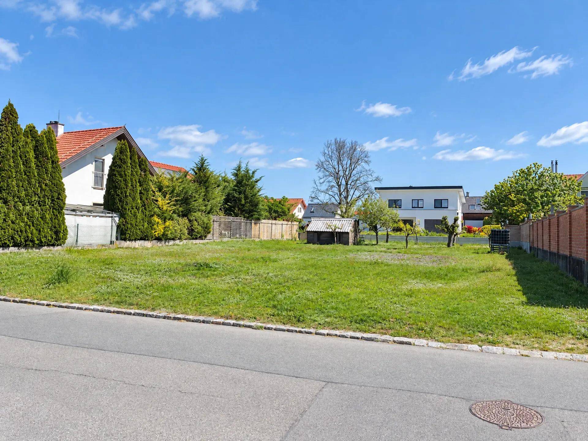Großes, unbebautes Grundstück mit Rasenfläche und angrenzenden Häusern in sonniger Lage.
