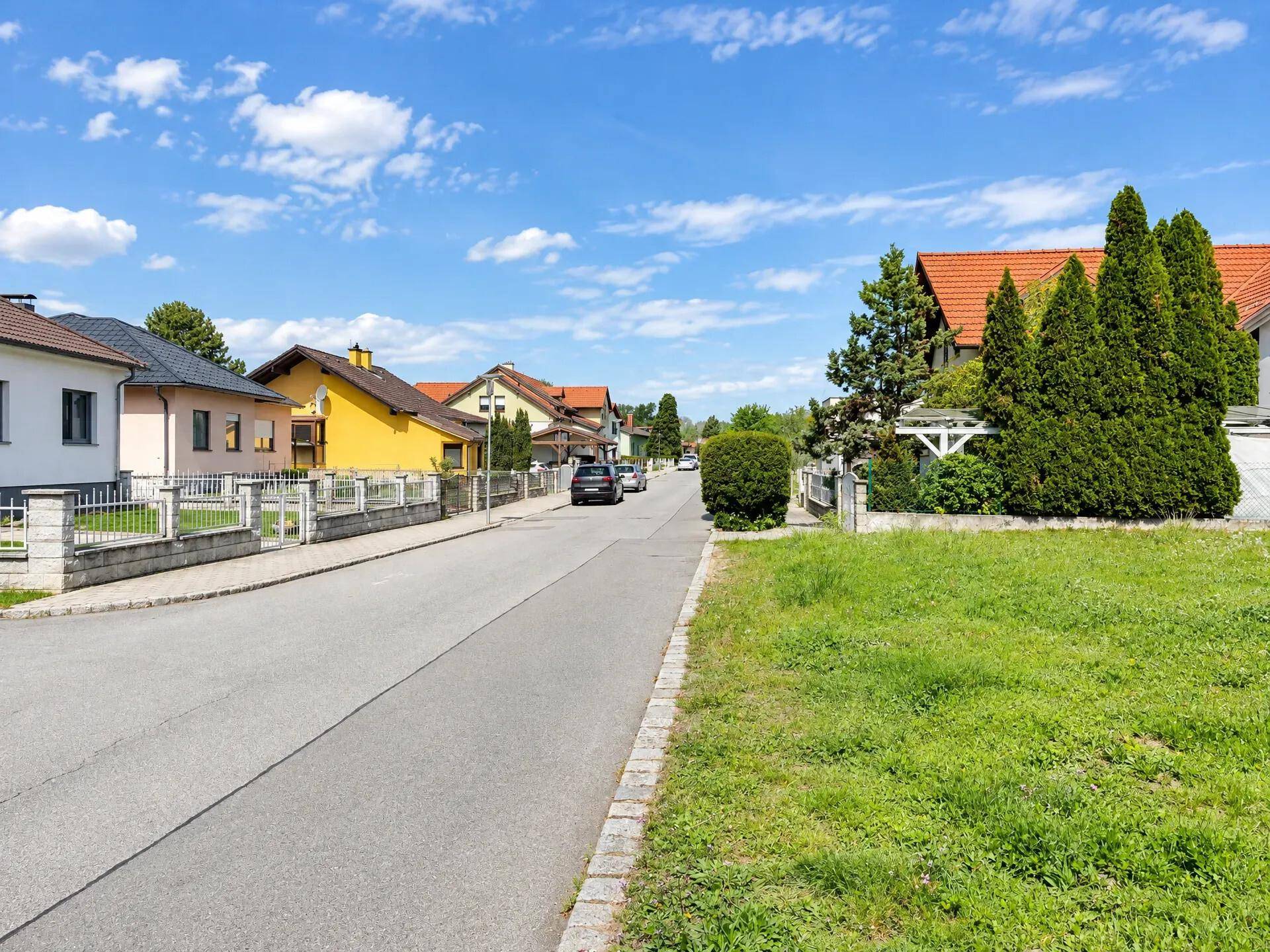 Ruhige Wohnstraße mit gepflegten Häusern und grünen Vorgärten unter blauem Himmel.