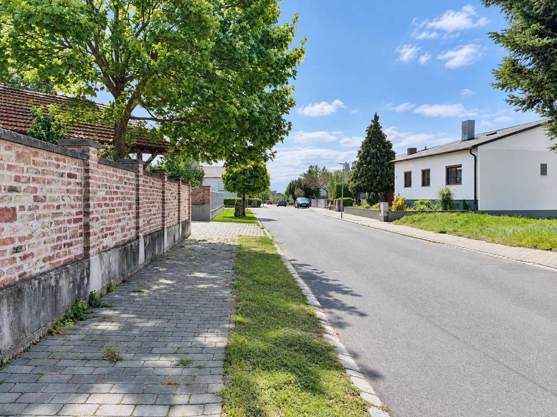 Wohnstraße mit altem Baumbestand und einer traditionellen Ziegelmauer entlang des Gehwegs.