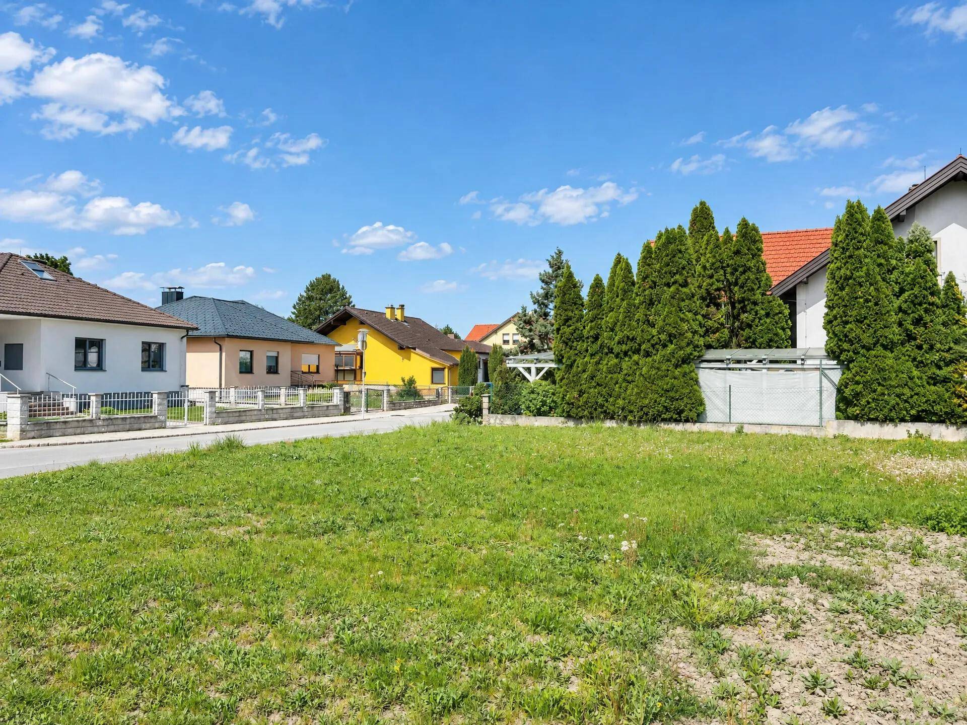 Unbebautes Grundstück mit Rasenfläche und Blick auf die Nachbarschaftshäuser in sonniger Umgebung.