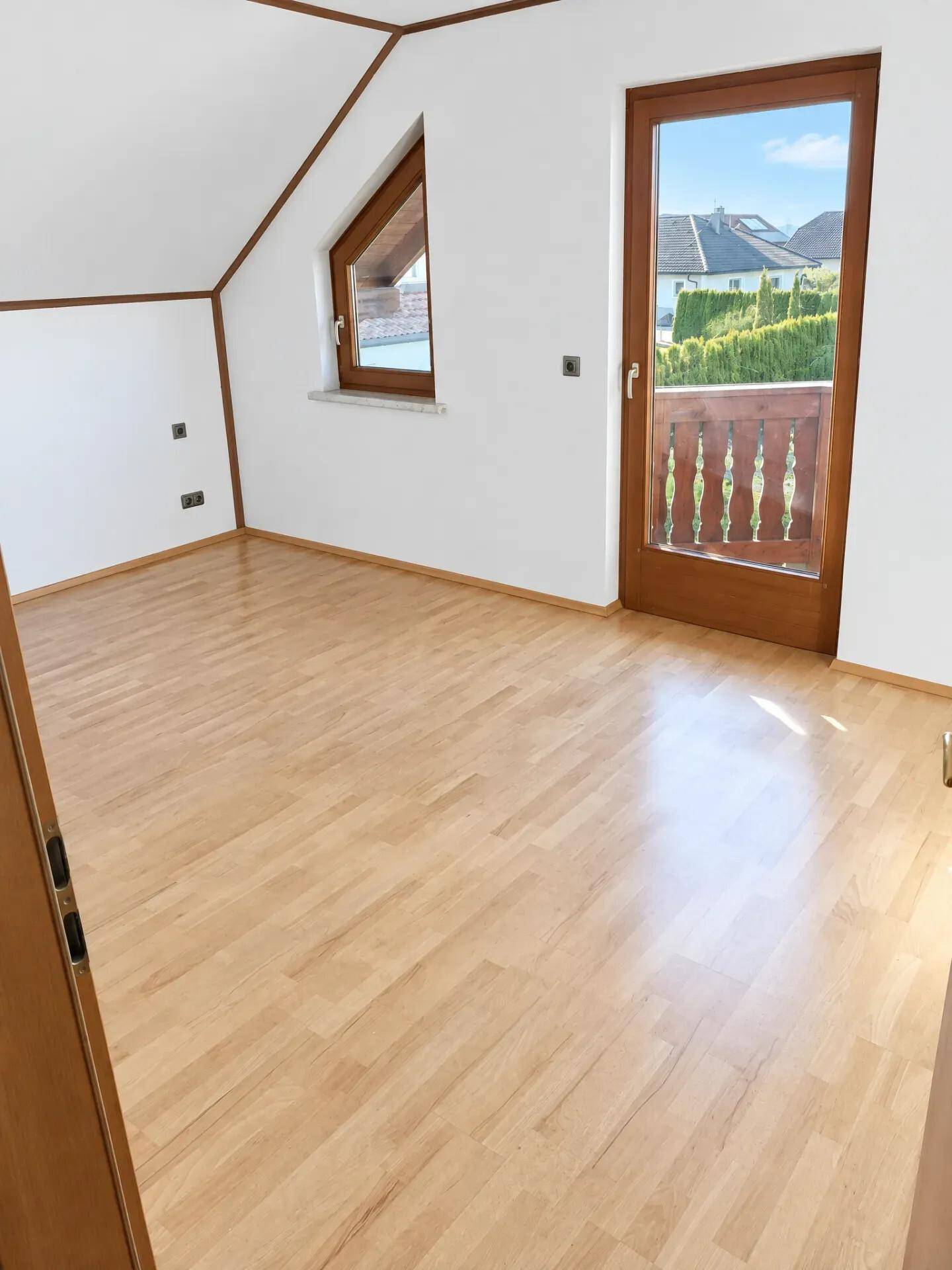Helles Schlafzimmer mit Holzboden, Dachschräge, Dachfenster und Zugang zu einem kleinen Balkon.