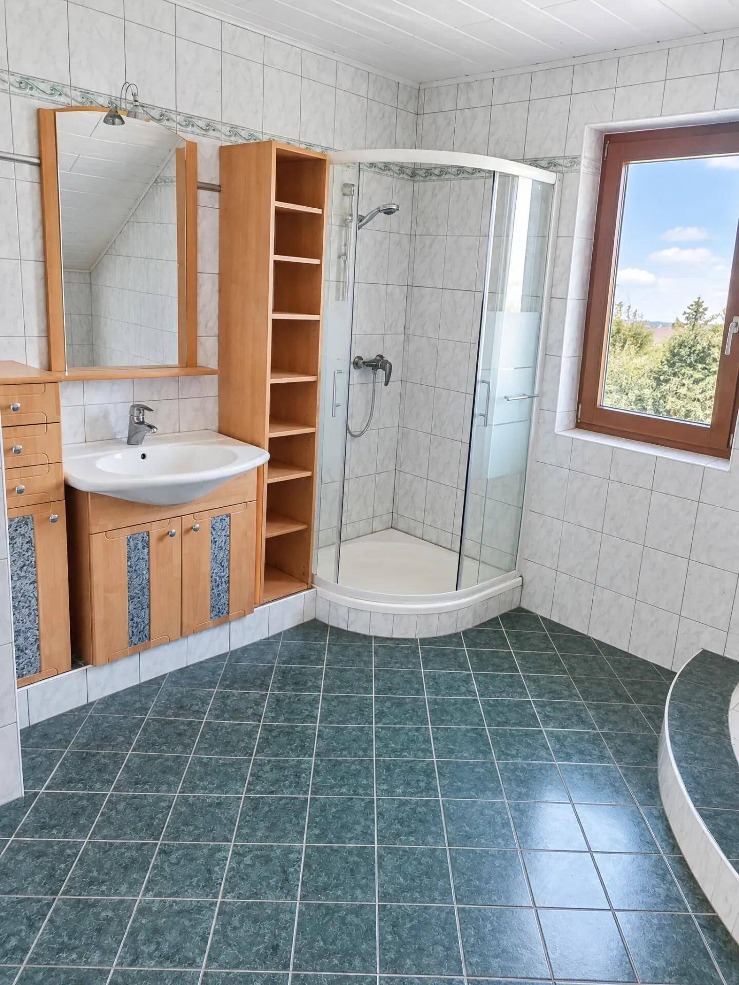 Badezimmer mit Eckdusche, Einzelwaschbecken, Fenster und grünen Bodenfliesen.