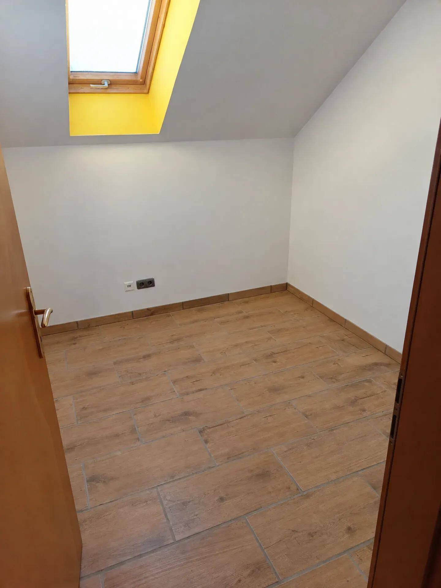 Kleines Zimmer mit Dachschräge, Dachfenster und Fliesen in Holzoptik.