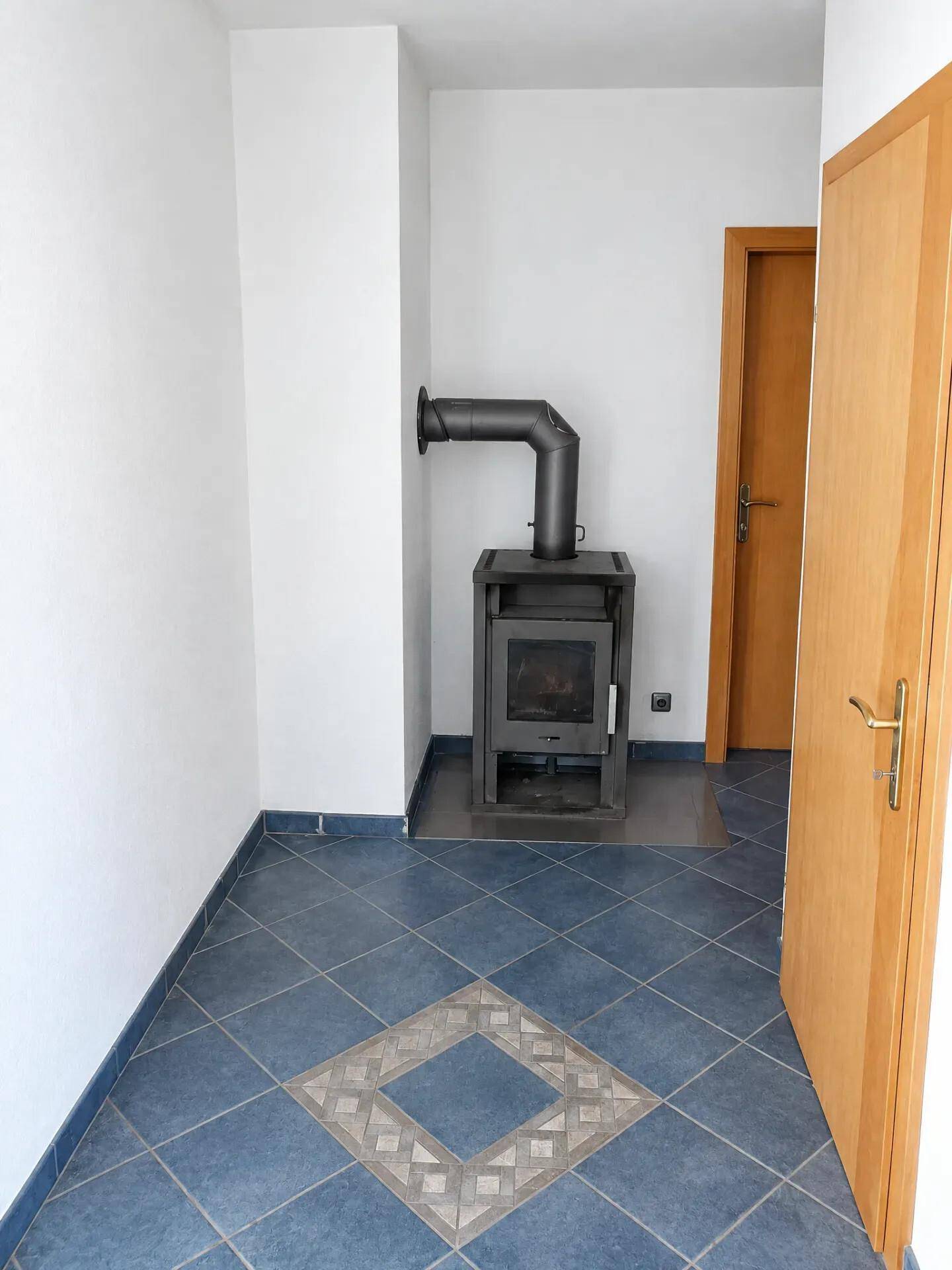 Kleiner Raum mit blauen Fliesenboden und einem modernen Holzofen.