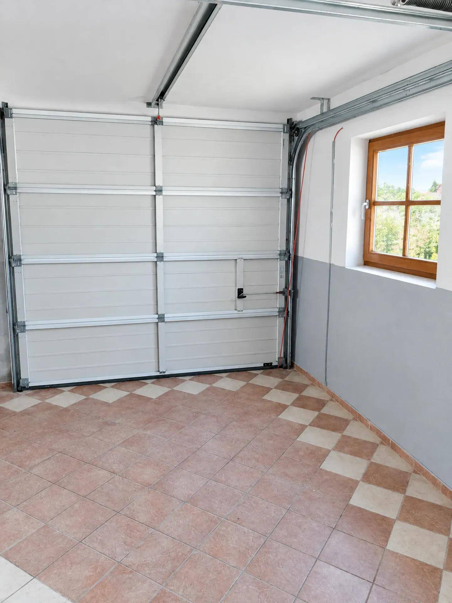 Geräumige Garage mit Sektionaltor, Fenster und kariertem Fliesenboden.