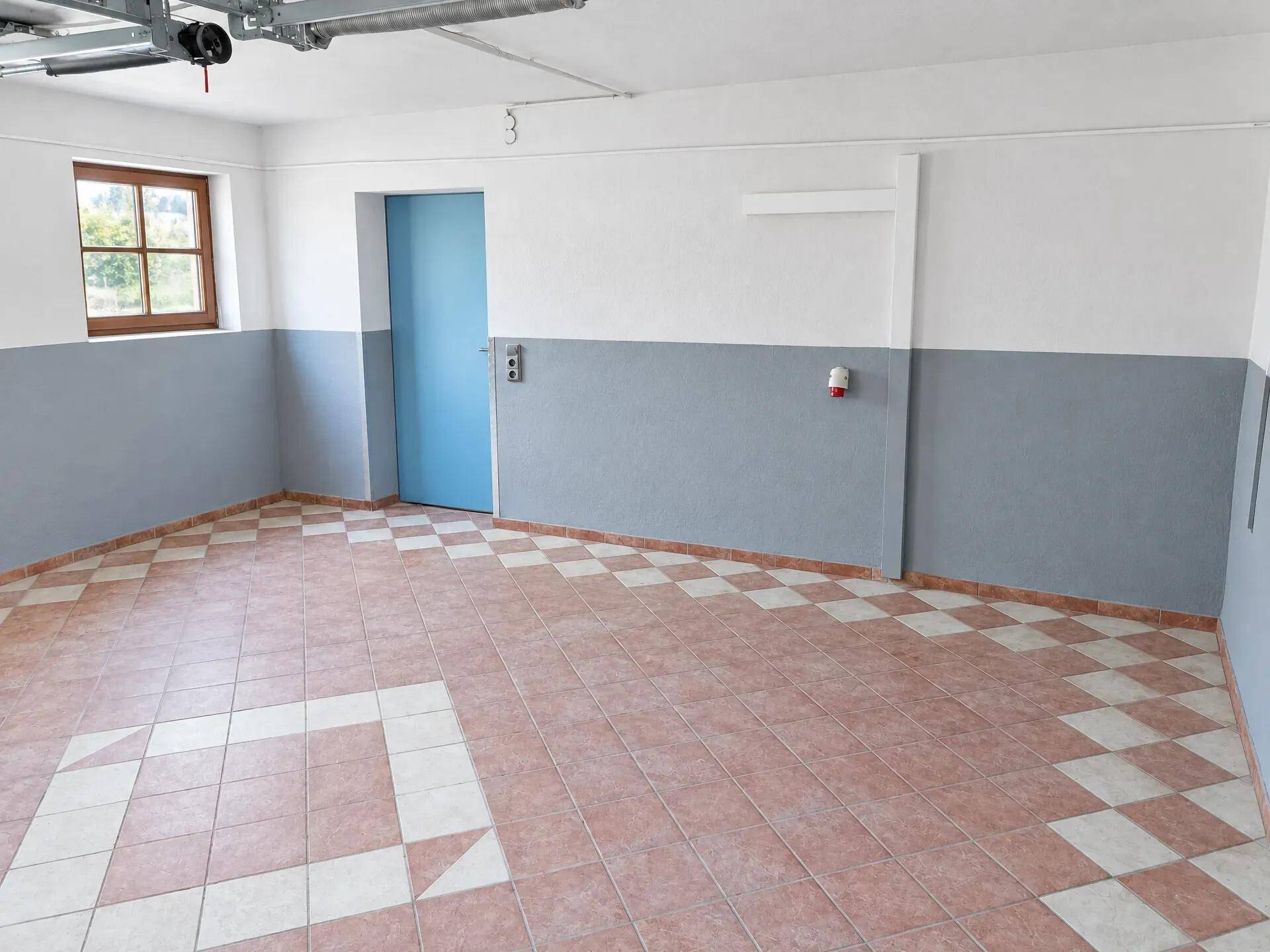 Innenansicht der Garage mit blauem Zugangstor und Fenster.
