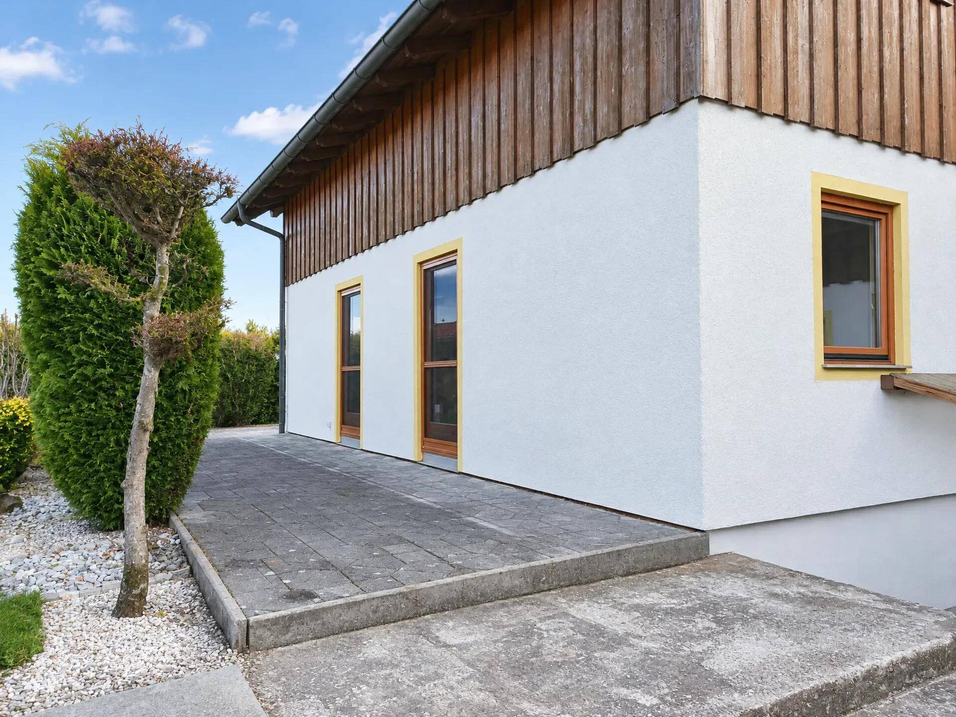 Seitenansicht des Hauses mit gepflastertem Weg, Holzverkleidung und gepflegter Bepflanzung.