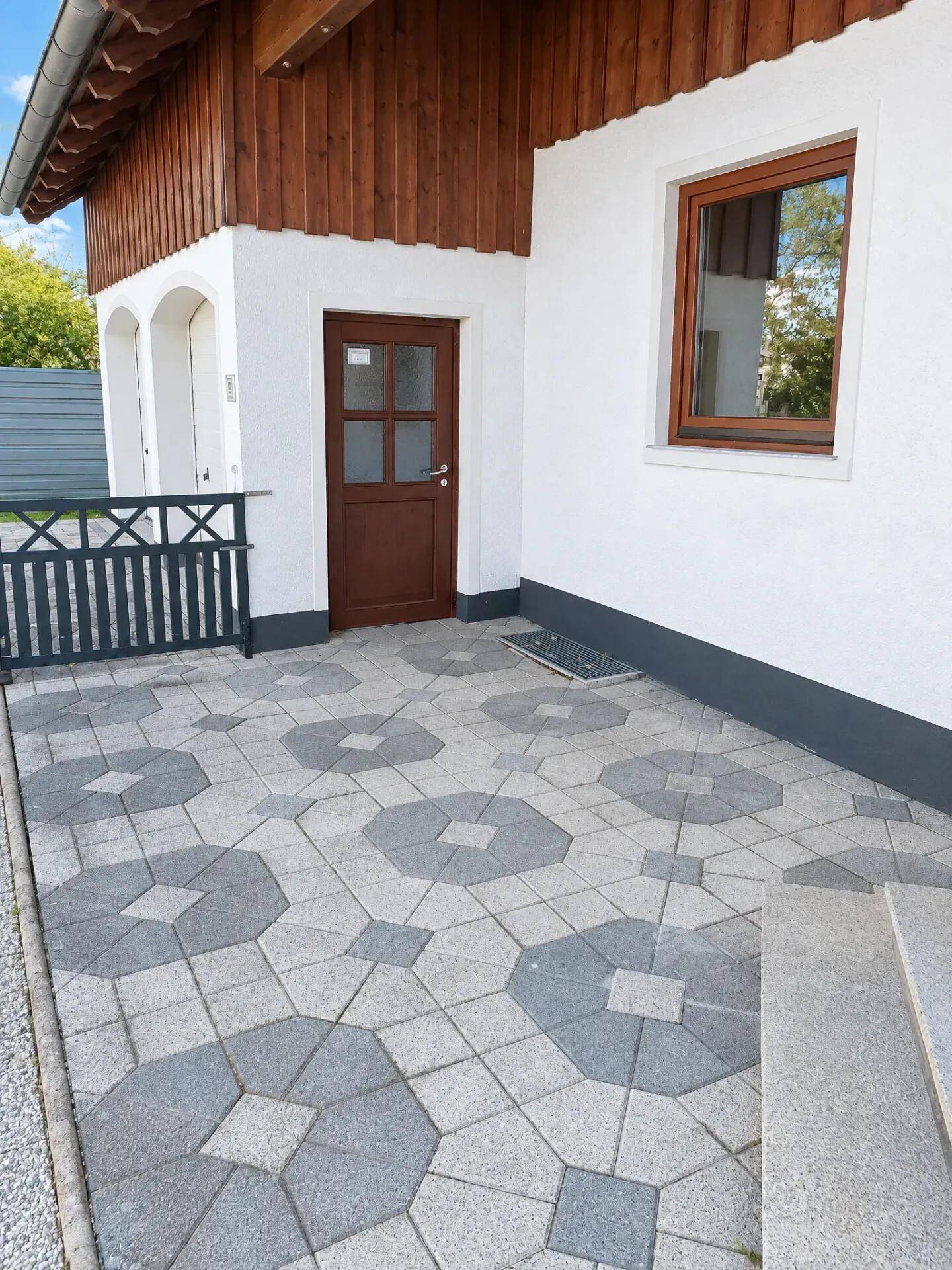 Eingangsbereich des Hauses mit gemustertem Pflaster und Holztür.