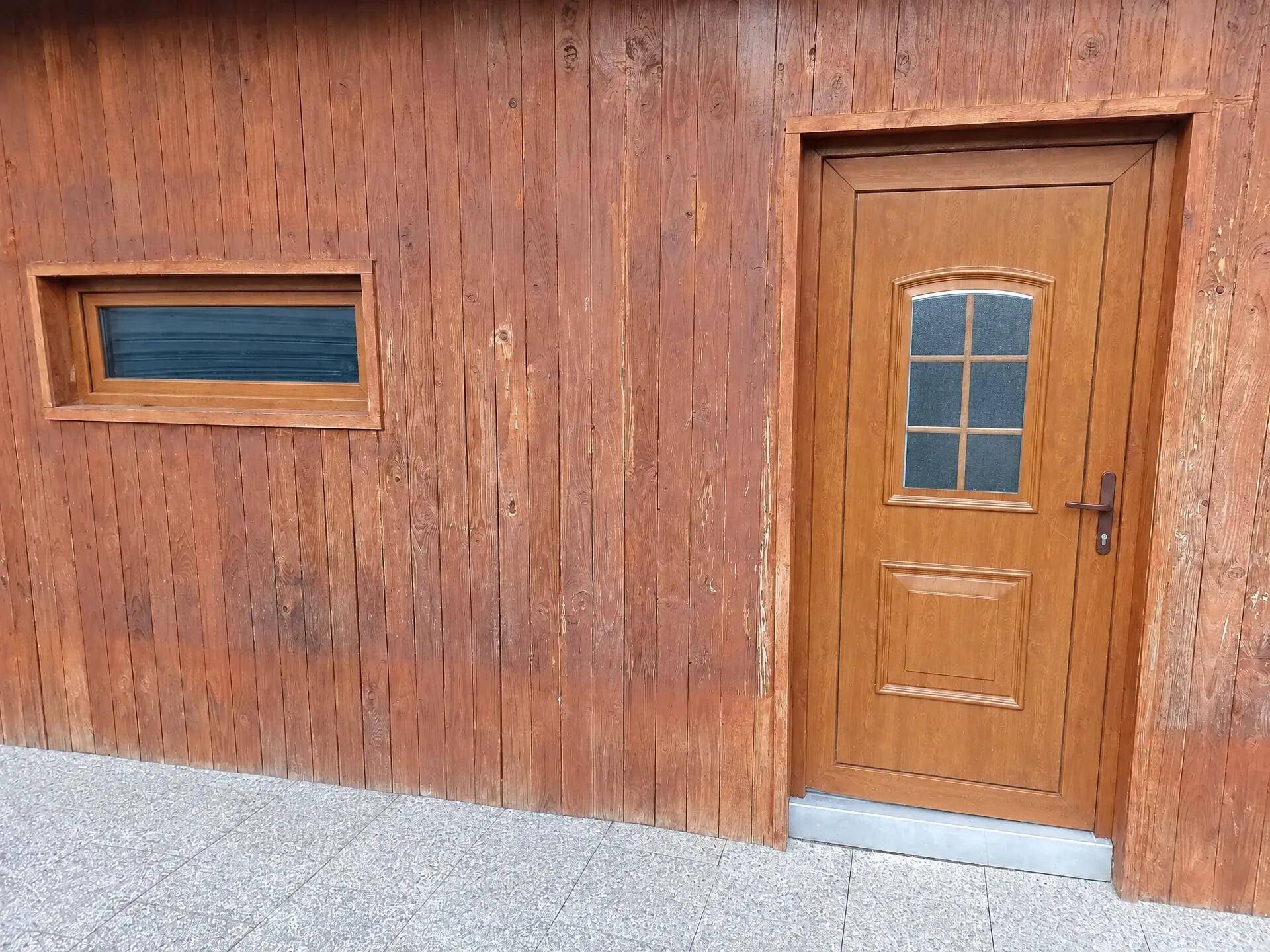 Holzverkleidete Fassade mit Holztür und kleinem Fenster.