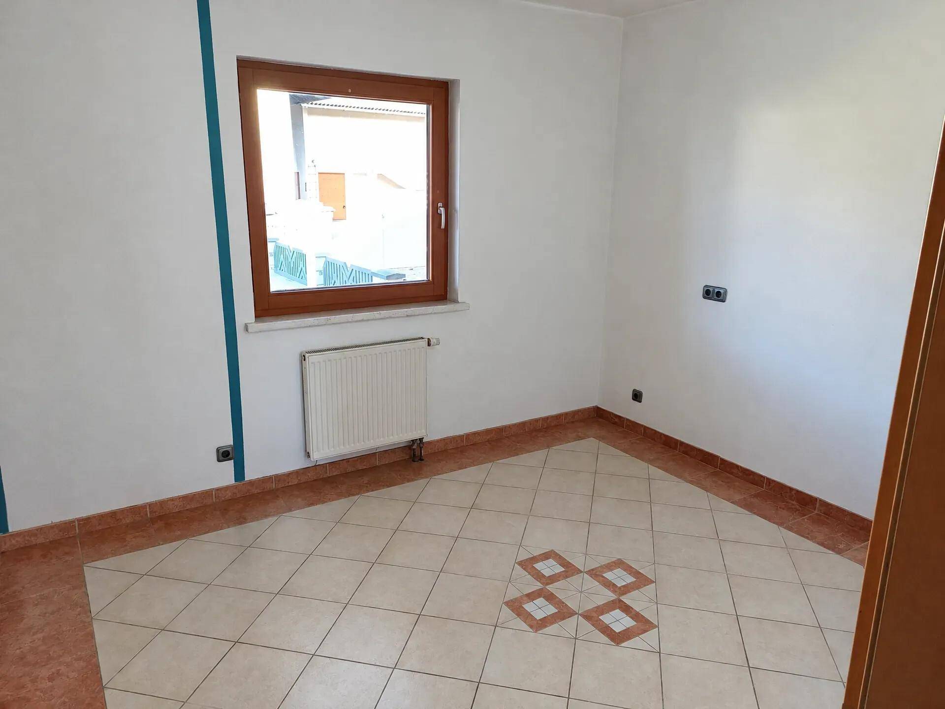 Helles Zimmer mit Fliesenboden, Fenster und Heizkörper.