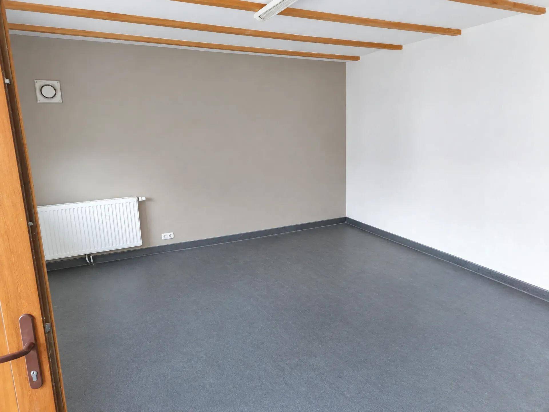 Leerer Raum mit grauem Boden, Heizkörper und sichtbaren Holzdeckenbalken.