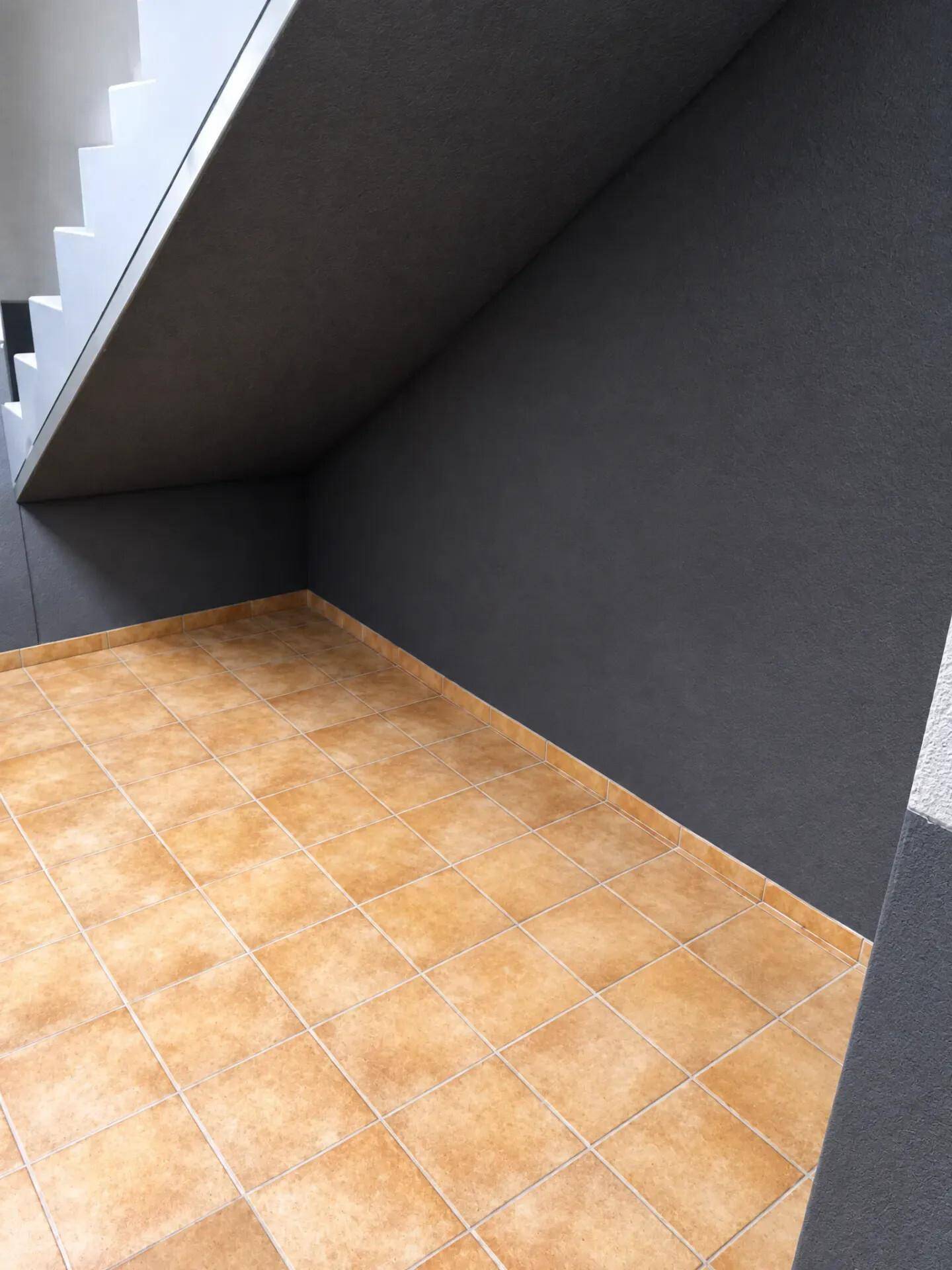 Gefliester Bereich unter einer Treppe mit dunkler Wand.