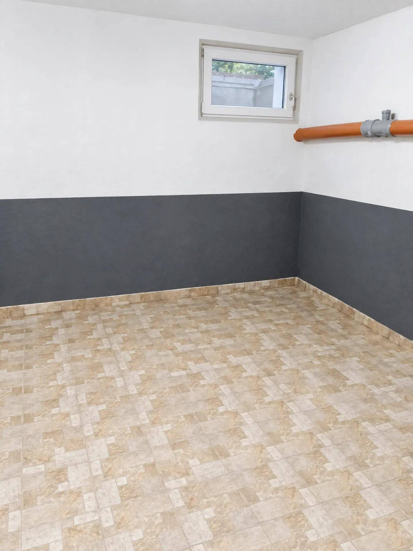 Hauswirtschaftsraum mit gemustertem Fliesenboden, Fenster und sichtbarer Rohrleitung.