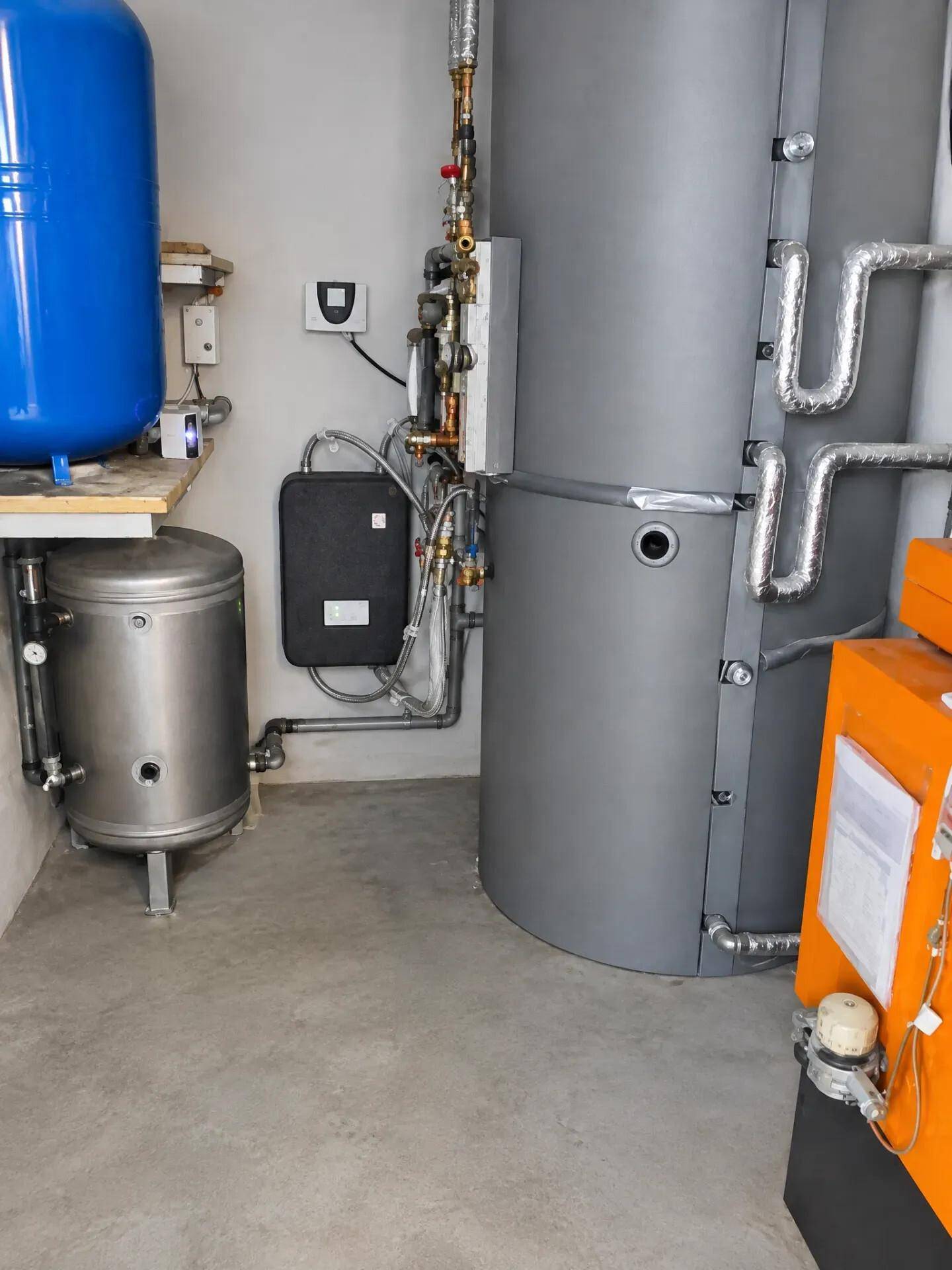 Technikraum mit Heizungsanlage, Warmwasserspeicher und umfangreichen Rohrleitungen für das Gebäude.