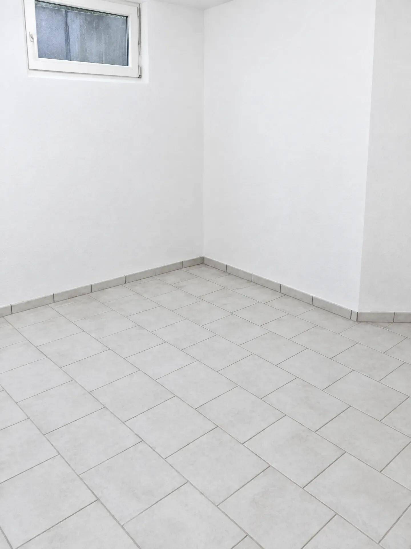 Heller Raum im Untergeschoss mit Fliesenboden und kleinem Fenster für natürliche Belichtung.
