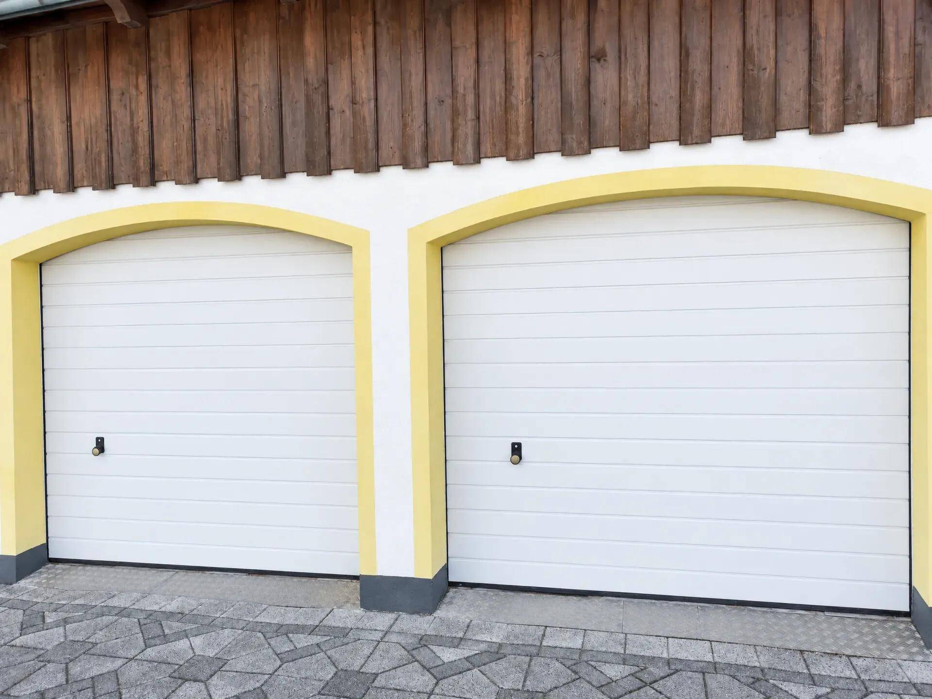 Doppelgarage mit zwei weißen Toren, gelben Bögen und einer Holzverkleidung oberhalb des Eingangs.