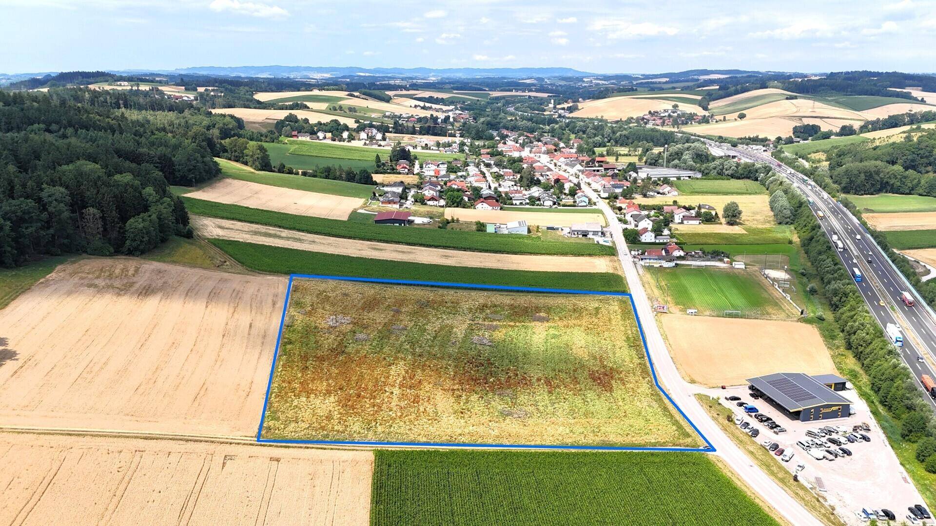 Luftaufnahme des blau umrandeten Grundstücks, eines Dorfes, einer Autobahn und umliegender Felder und Wälder.