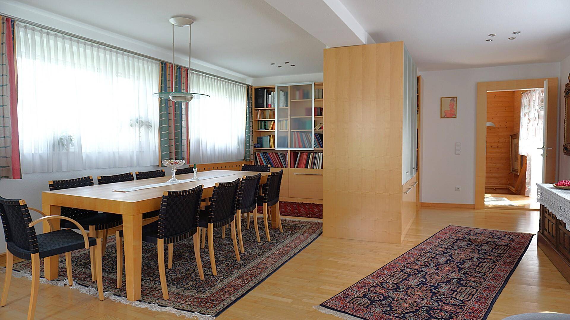 Geräumiger Essbereich mit großem Holztisch, Teppich und integriertem Bücherregal.
