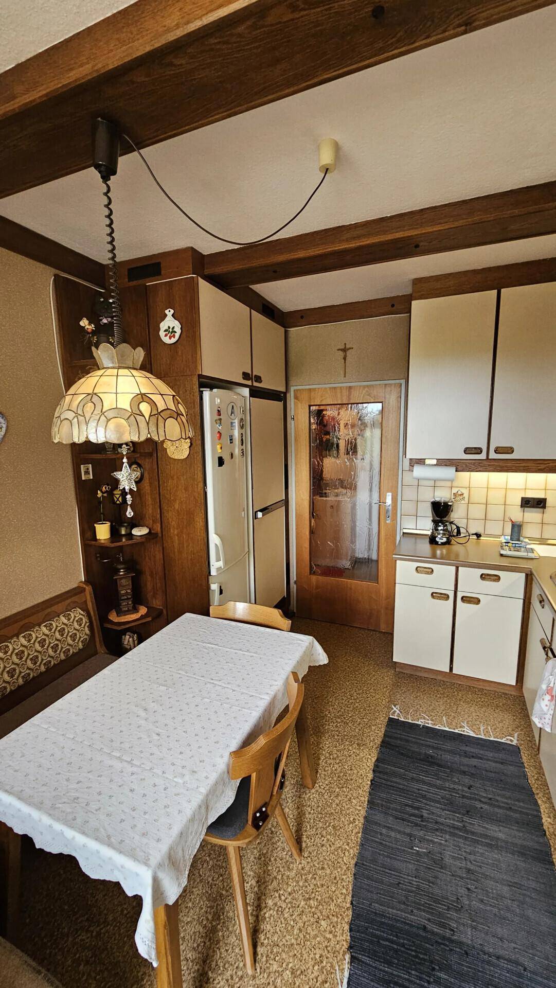 Gemütliche Küche mit Essbereich, Holzbalken an der Decke und Zugang zum Balkon.