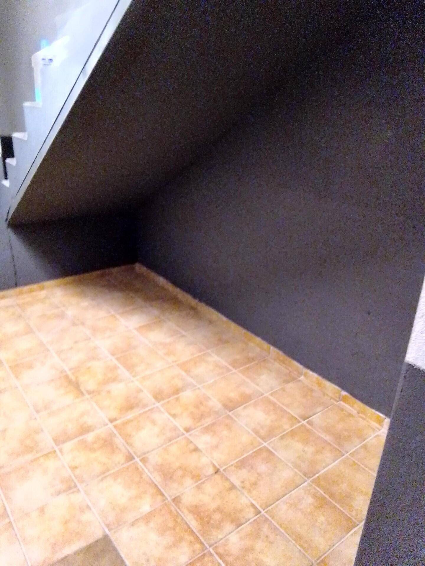 Bereich unter der Treppe mit Fliesenboden und dunkelgrau gestrichener Wand.