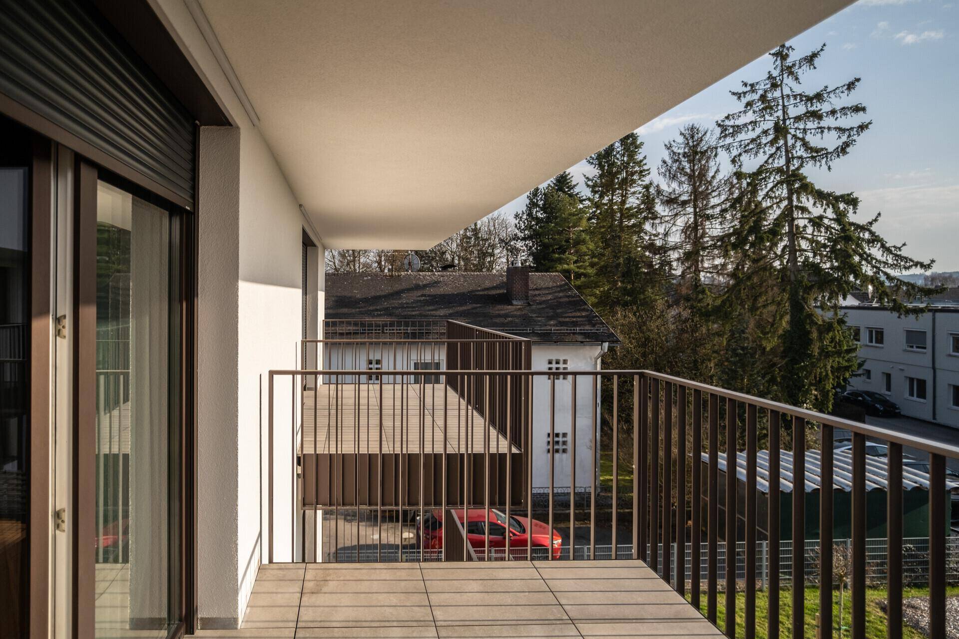 Geräumiger Balkon mit Fliesenboden und Blick auf die Umgebung mit Bäumen.