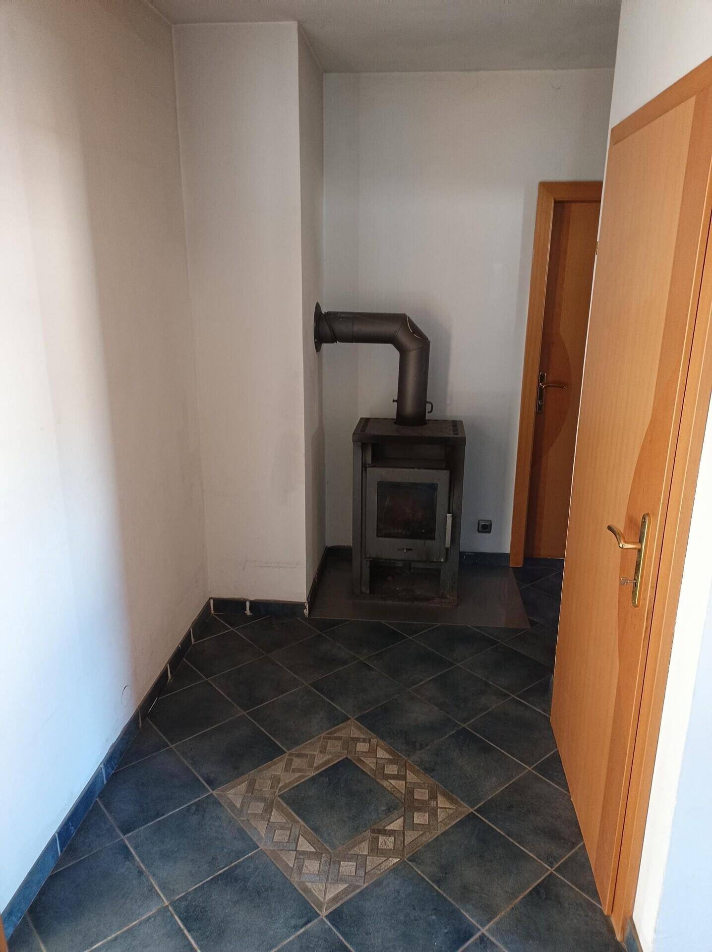 Kleiner Raum mit Fliesenboden und einem Holzofen, der für zusätzliche Wärme sorgt.