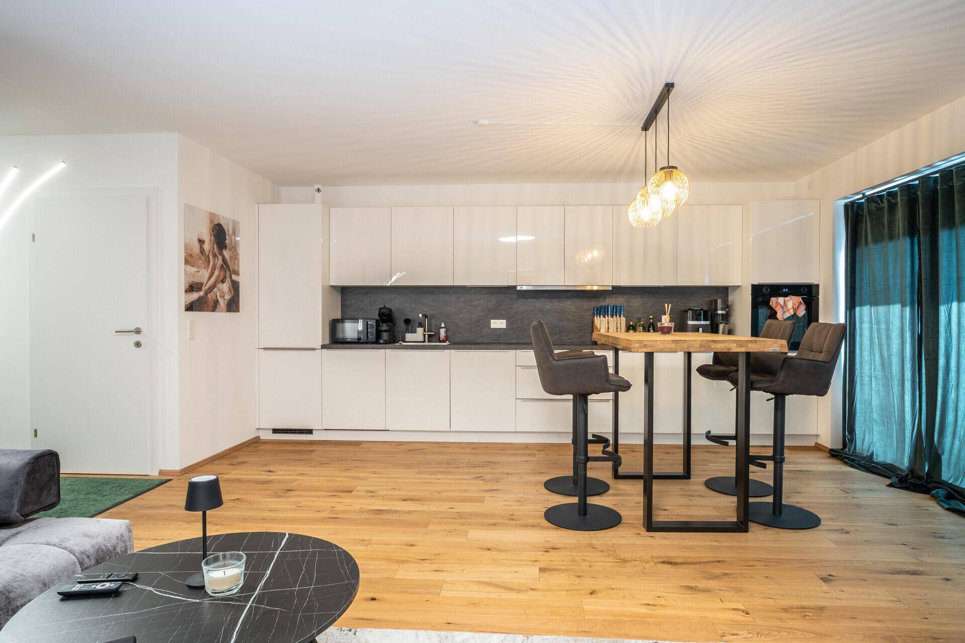 Offener Wohnbereich mit moderner Küche, Bartresen und bequemer Couch im Hintergrund.