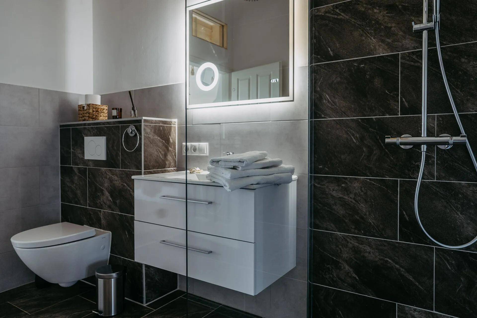 Modernes Badezimmer mit dunklen Fliesen, Waschtisch und geräumiger Duschkabine.