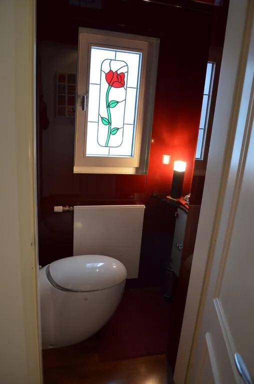 Kleines WC mit roter Wand, modernem WC und einem Buntglasfenster mit Blumenmotiv.