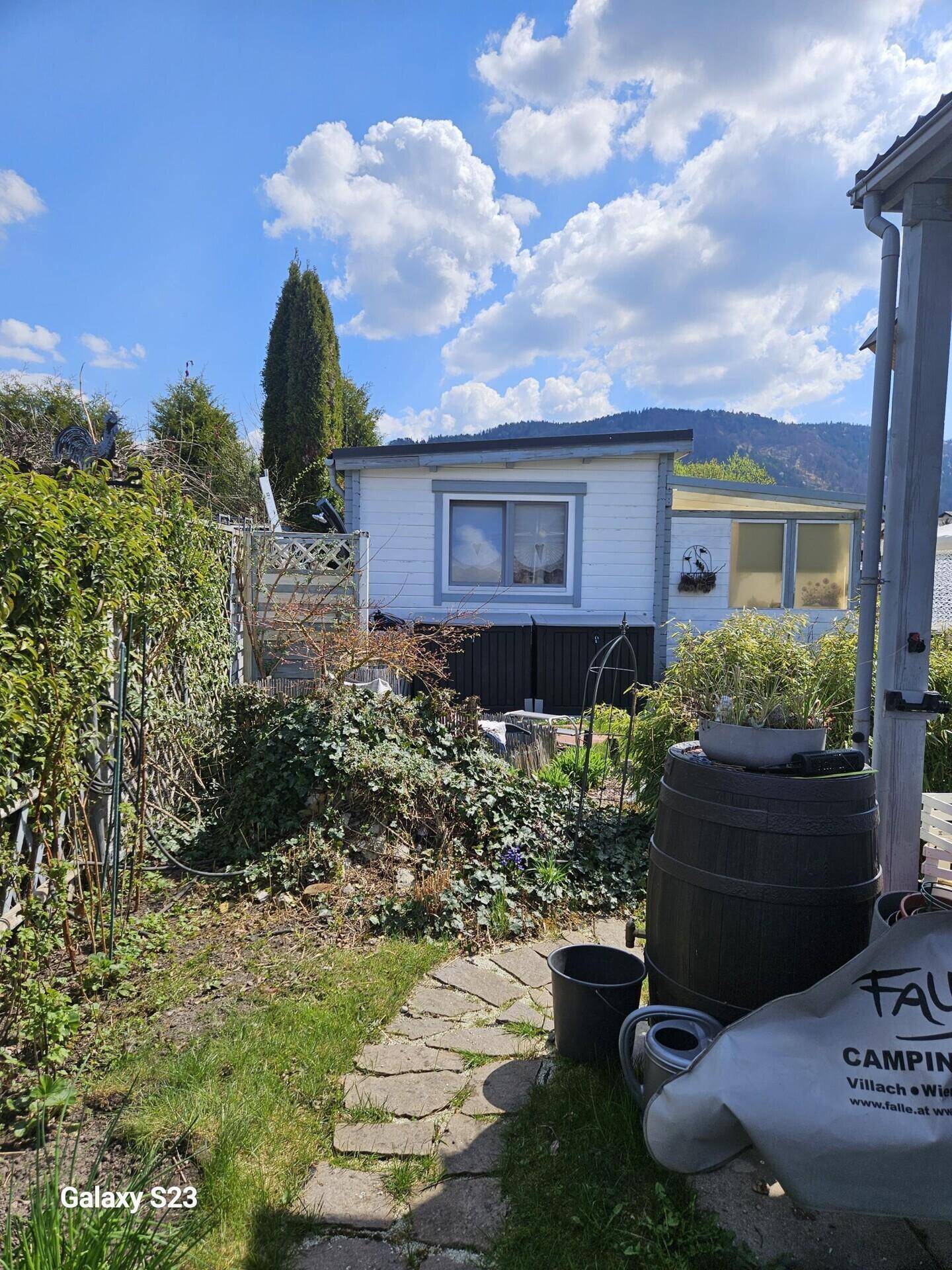 Hinterer Gartenbereich mit Steinweg, Pflanzen und Blick auf das kleine Holzhaus.