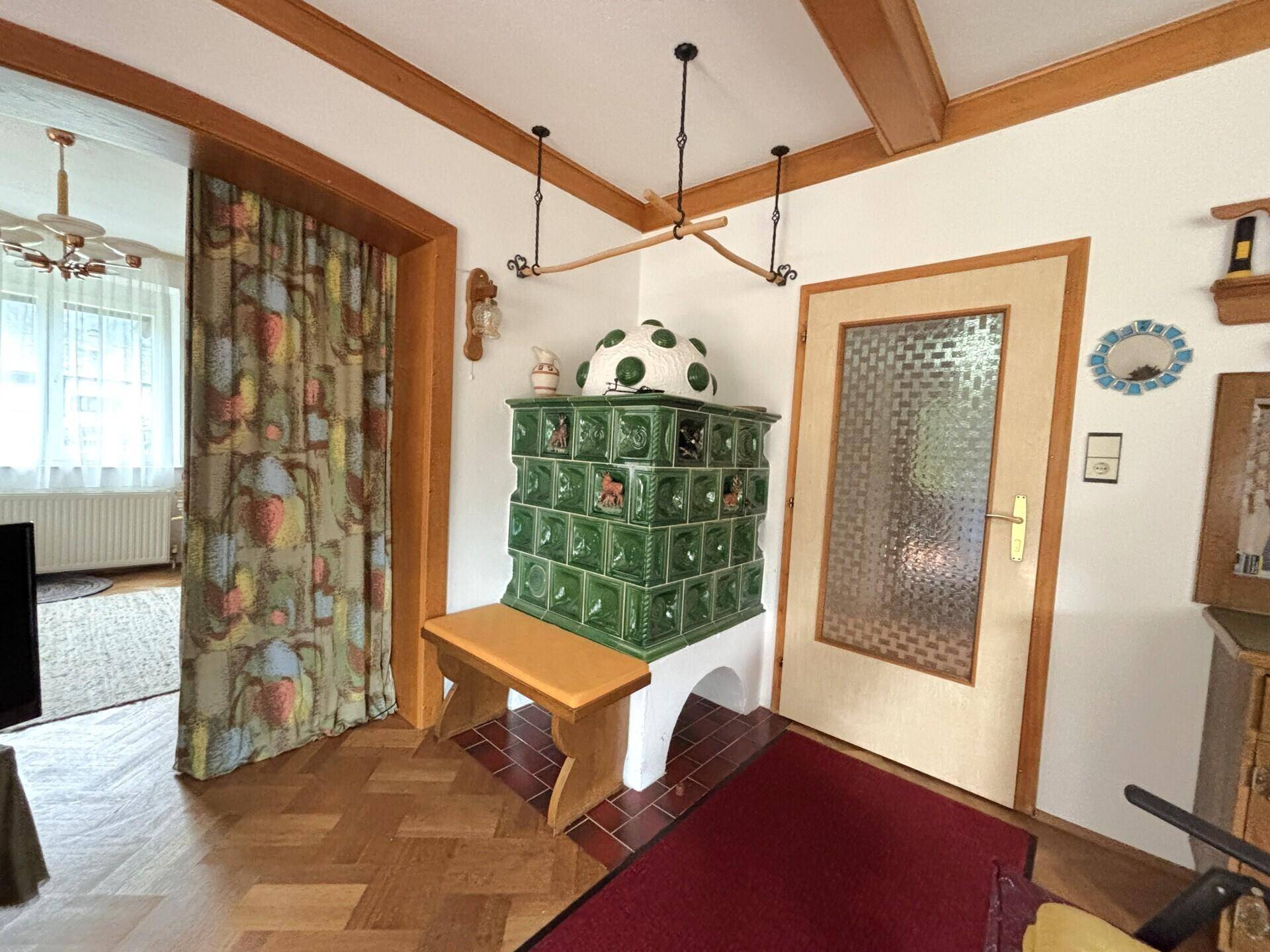 Eingangsbereich mit traditionellem Kachelofen, Holzbalken und Parkettboden.