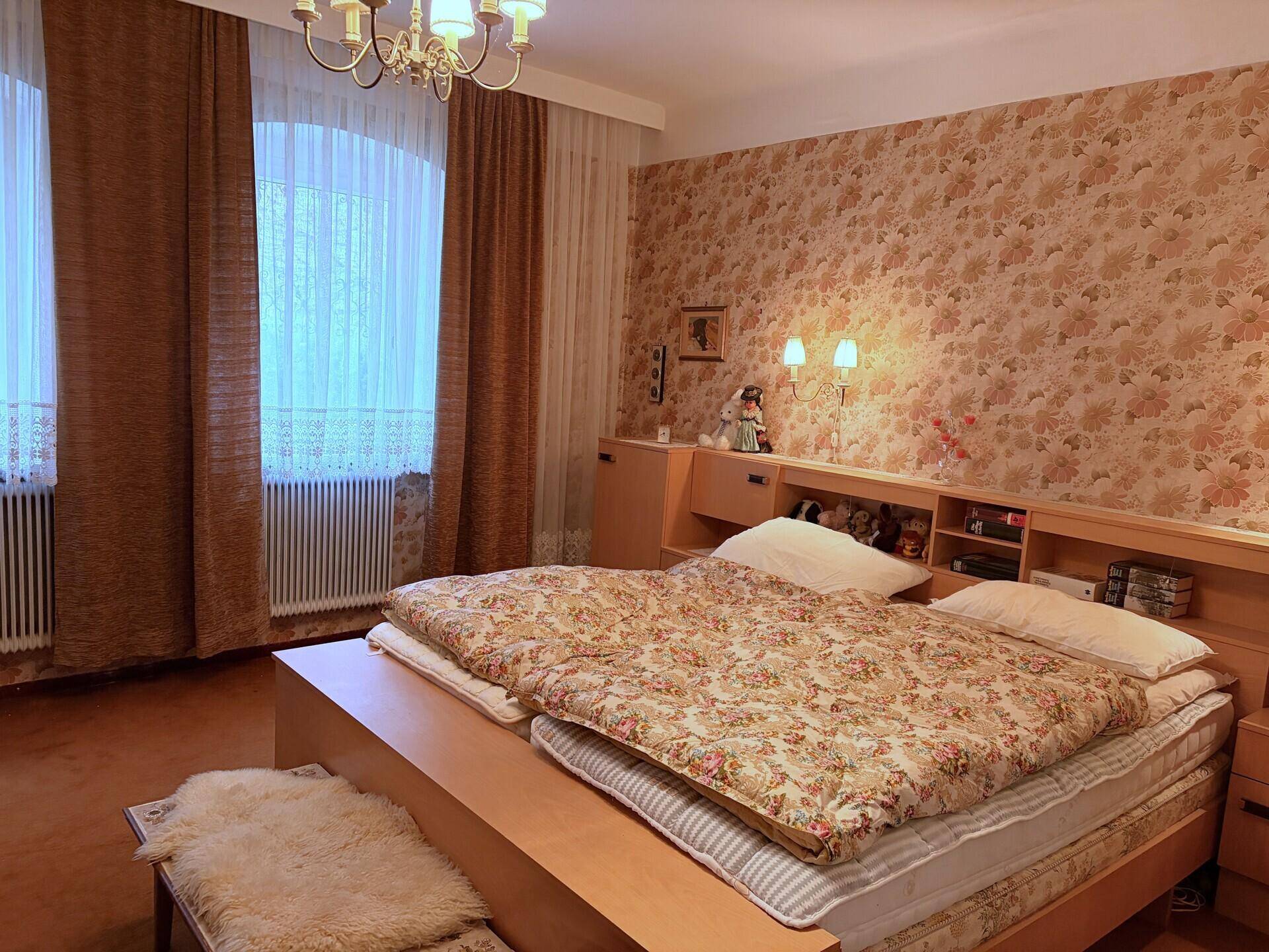 Schlafzimmer mit Doppelbett und gemusterter floraler Tapete.