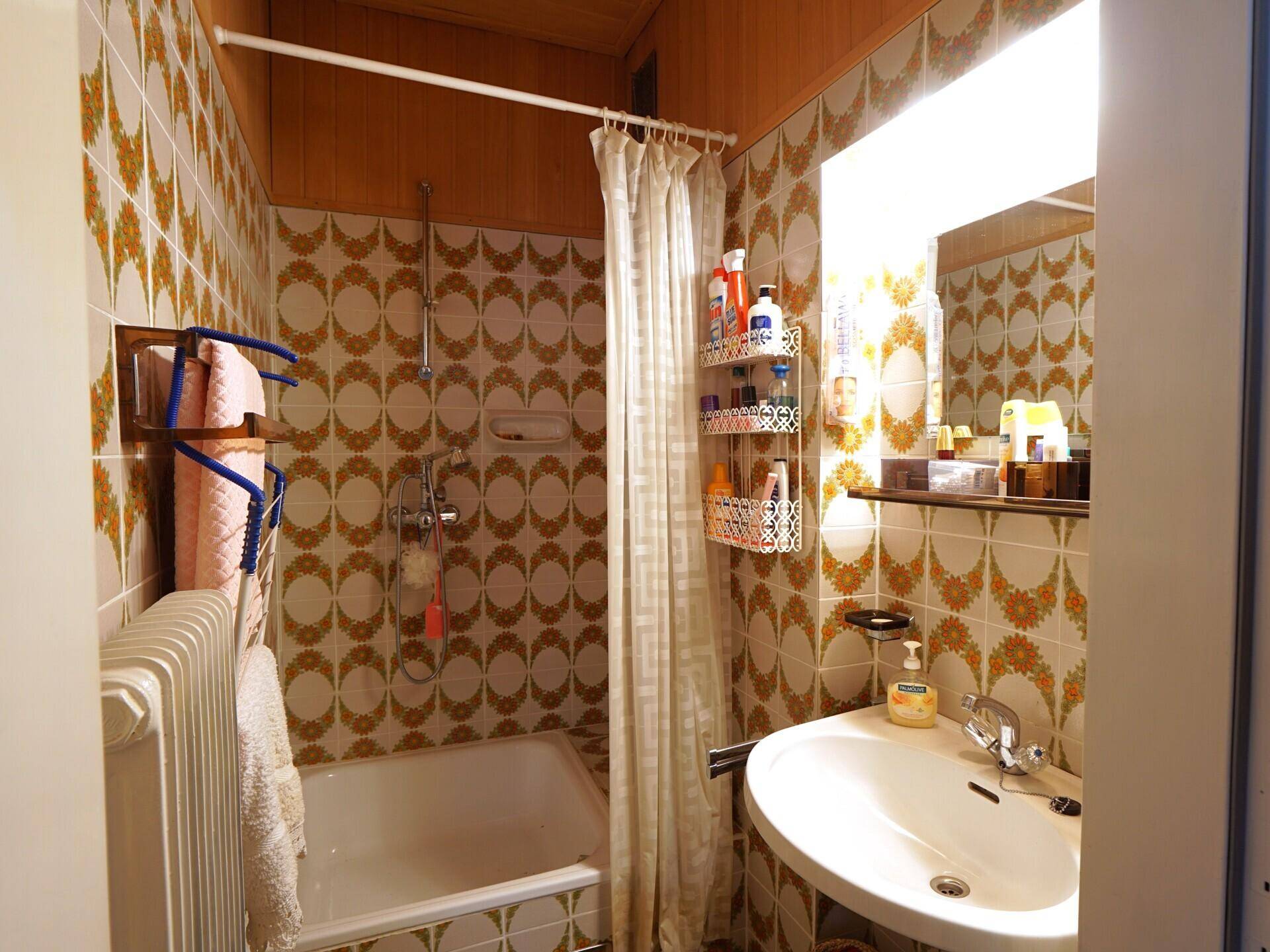 Badezimmer mit Badewanne, Dusche und Waschbecken, ausgestattet mit Fliesen im 70er-Jahre-Stil.