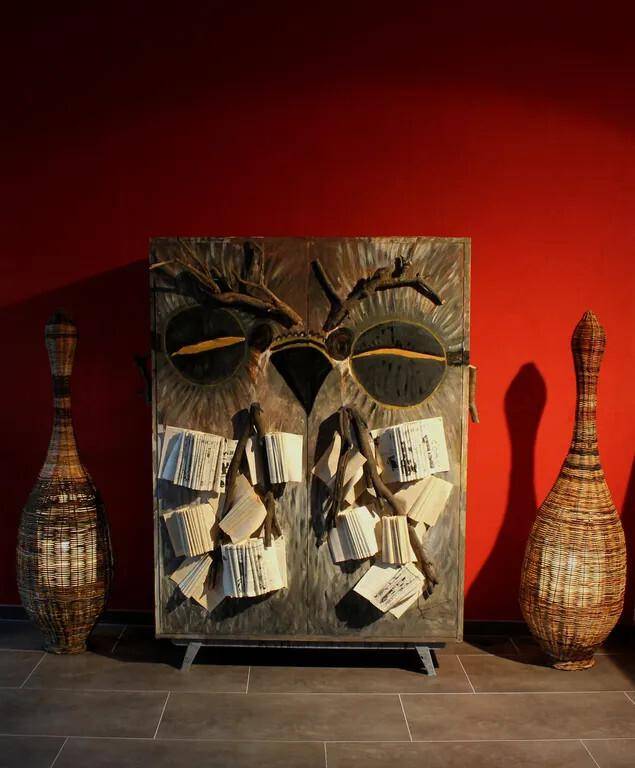Raum mit roter Wand und einem einzigartigen, kunstvollen Schrank, flankiert von hohen Vasen.