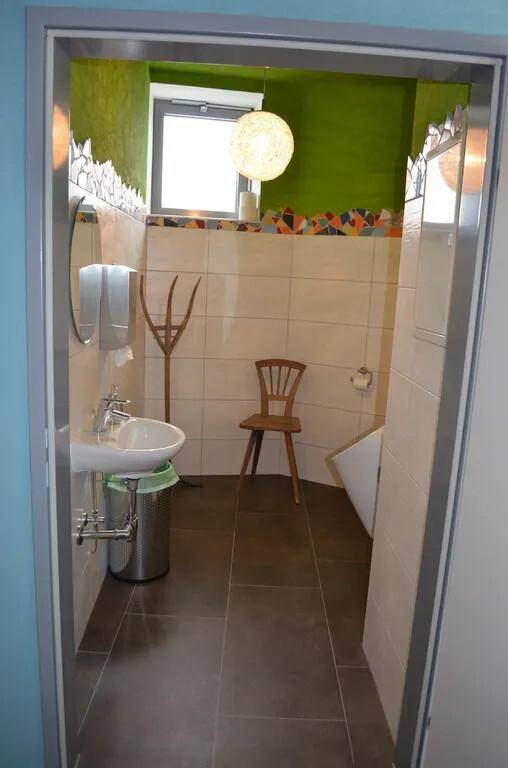 Helles Badezimmer mit Fenster, Waschbecken und farbenfrohen Fliesenbordüren.