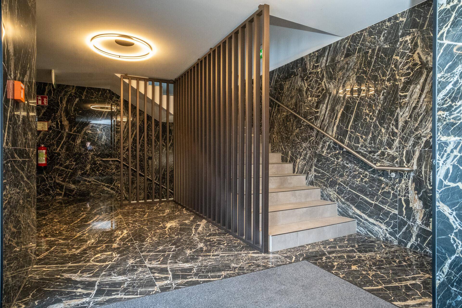Stilvoller Eingangsbereich mit schwarzem Marmorboden, Treppe und Holzlamellen als Raumteiler.