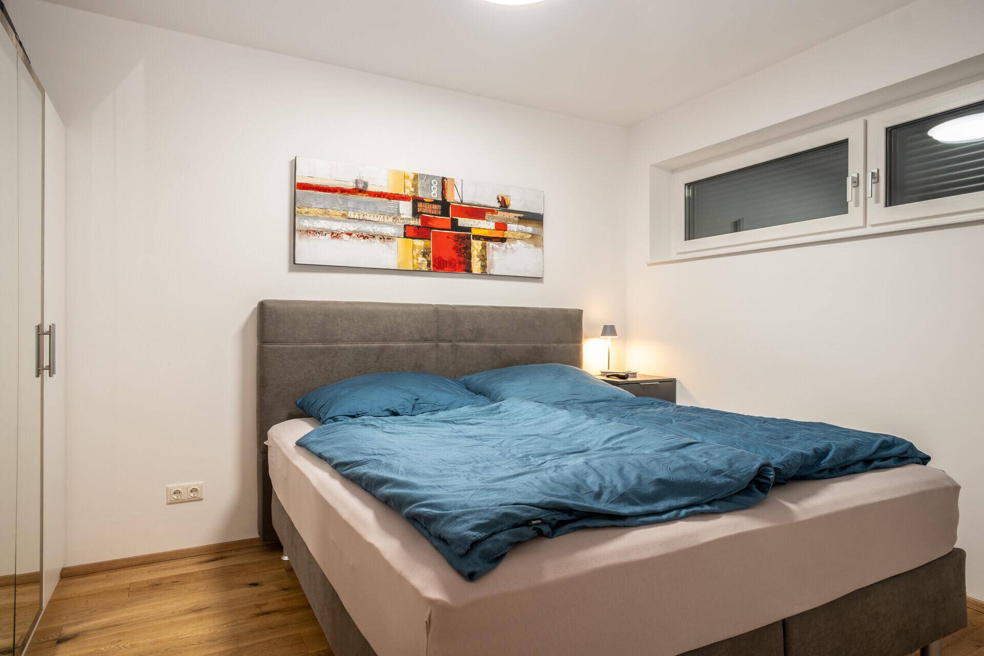 Schlafzimmer mit Doppelbett, Holzboden und Fenster für natürliches Licht.