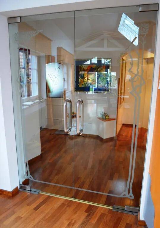 Eingangsbereich mit Holzboden und einer Glastür mit dekorativen Mustern.