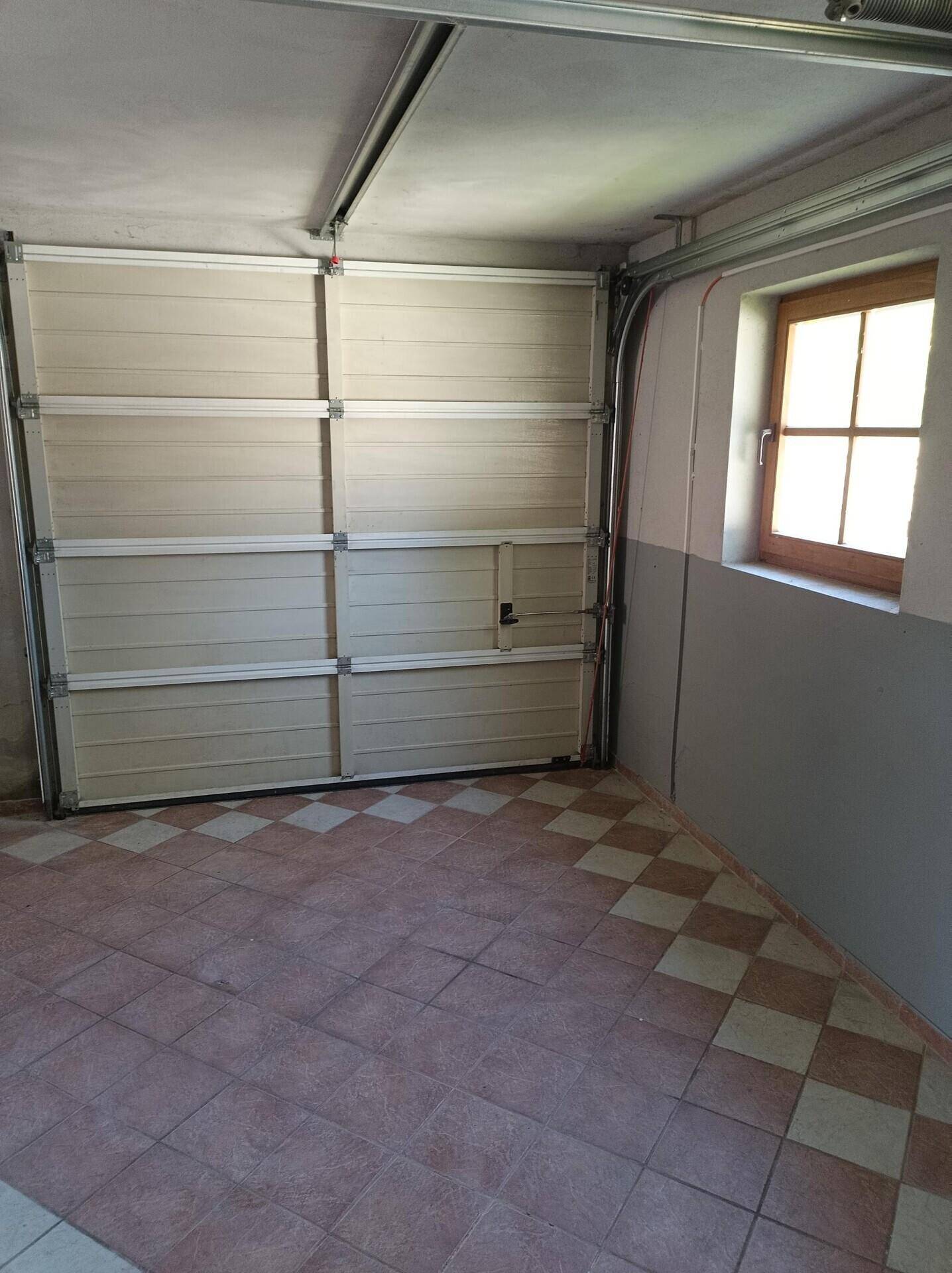 Innenansicht der Garage mit Sektionaltor, Fliesenboden und kleinem Fenster.
