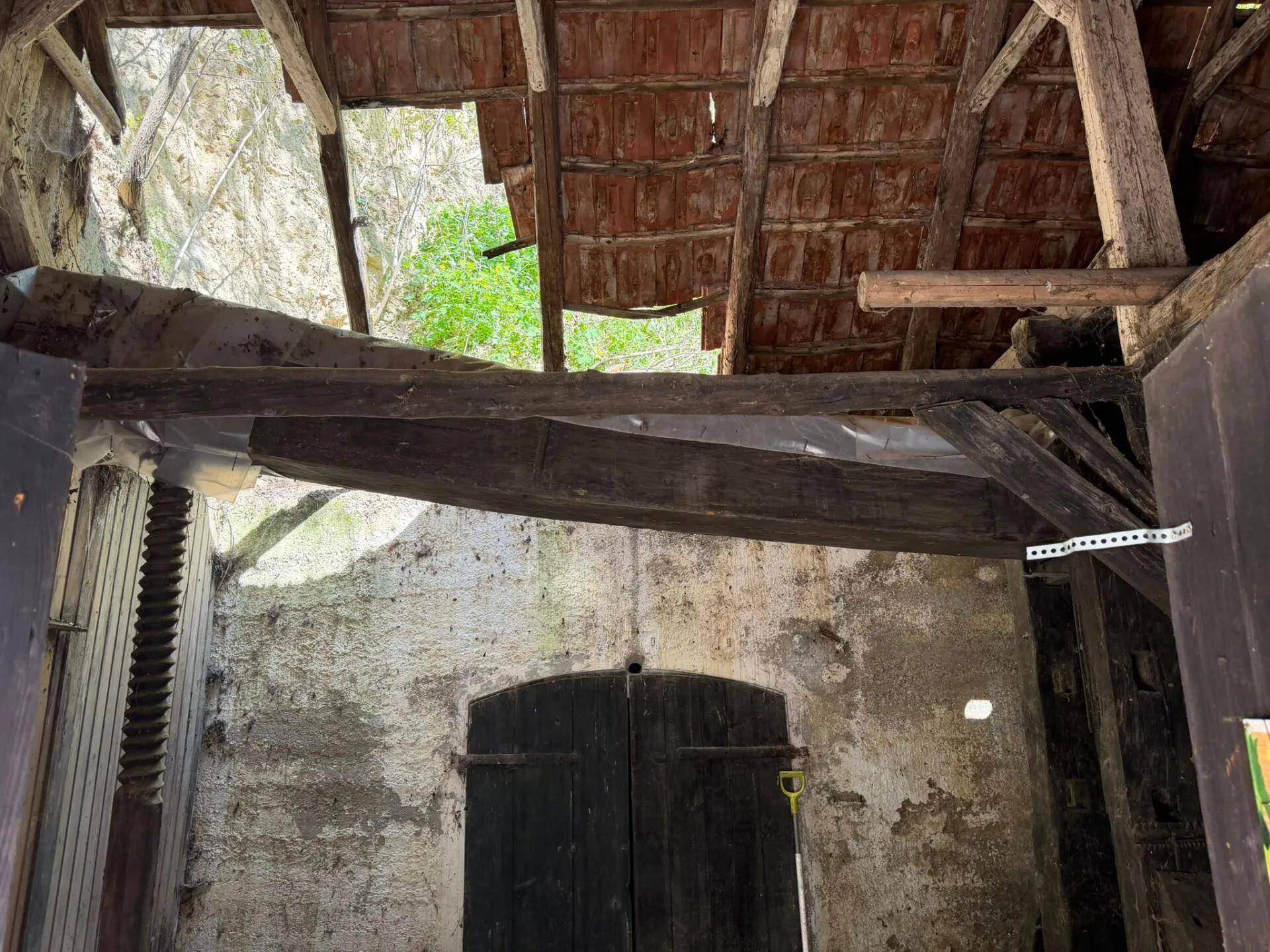 Innenansicht eines verfallenen Gebäudes mit freiliegenden Holzbalken und einem teilweise offenen Dach.