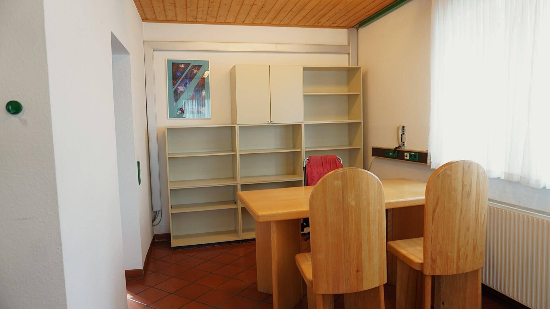 Helles Büro mit Schreibtisch, Stühlen und offenen Regalen.
