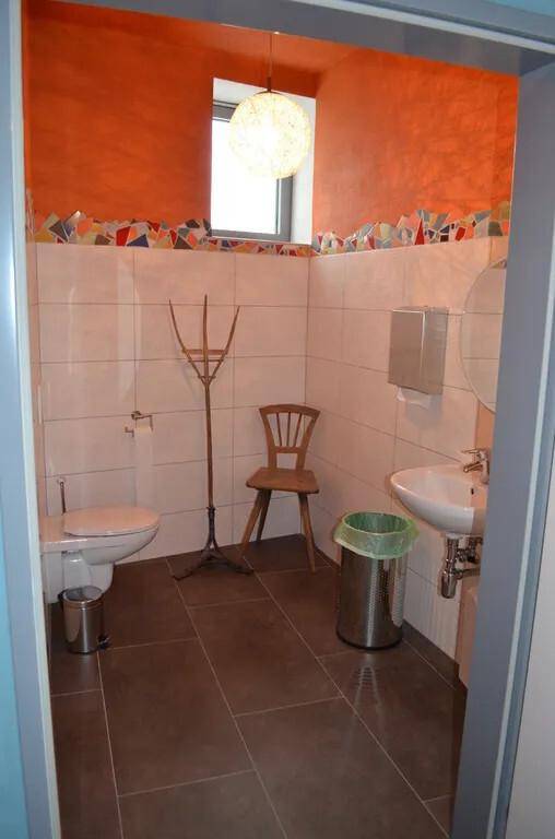 Gäste-WC mit Fenster, Wand-WC und farbenfroher Fliesenbordüre.