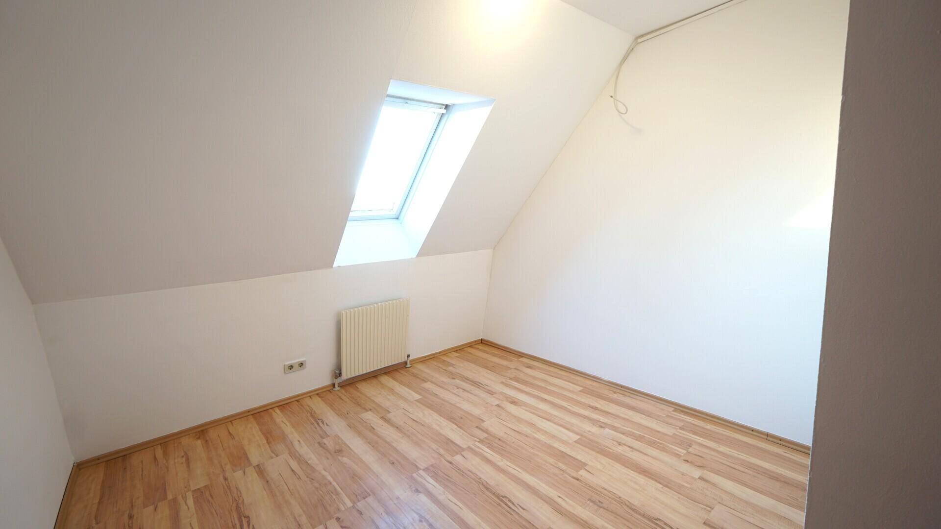 Helles Zimmer im Dachgeschoss mit Laminatboden und großem Dachfenster.