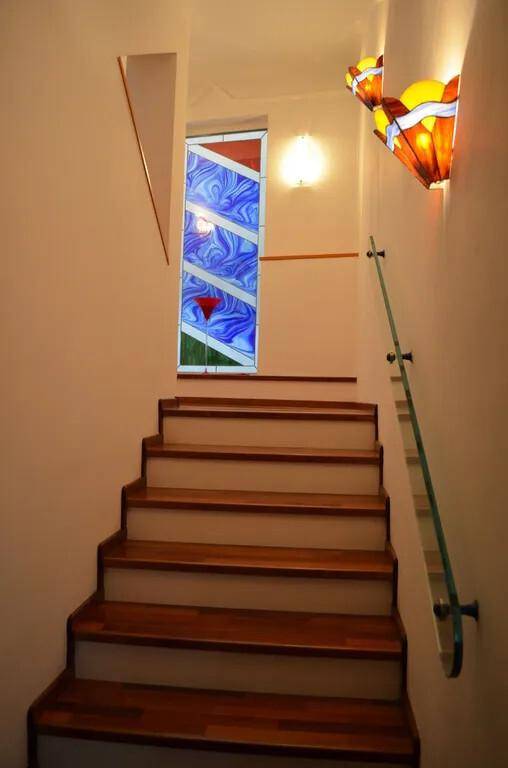Treppenhaus mit Holzstufen, Glasgeländer und einem farbigen Buntglasfenster.