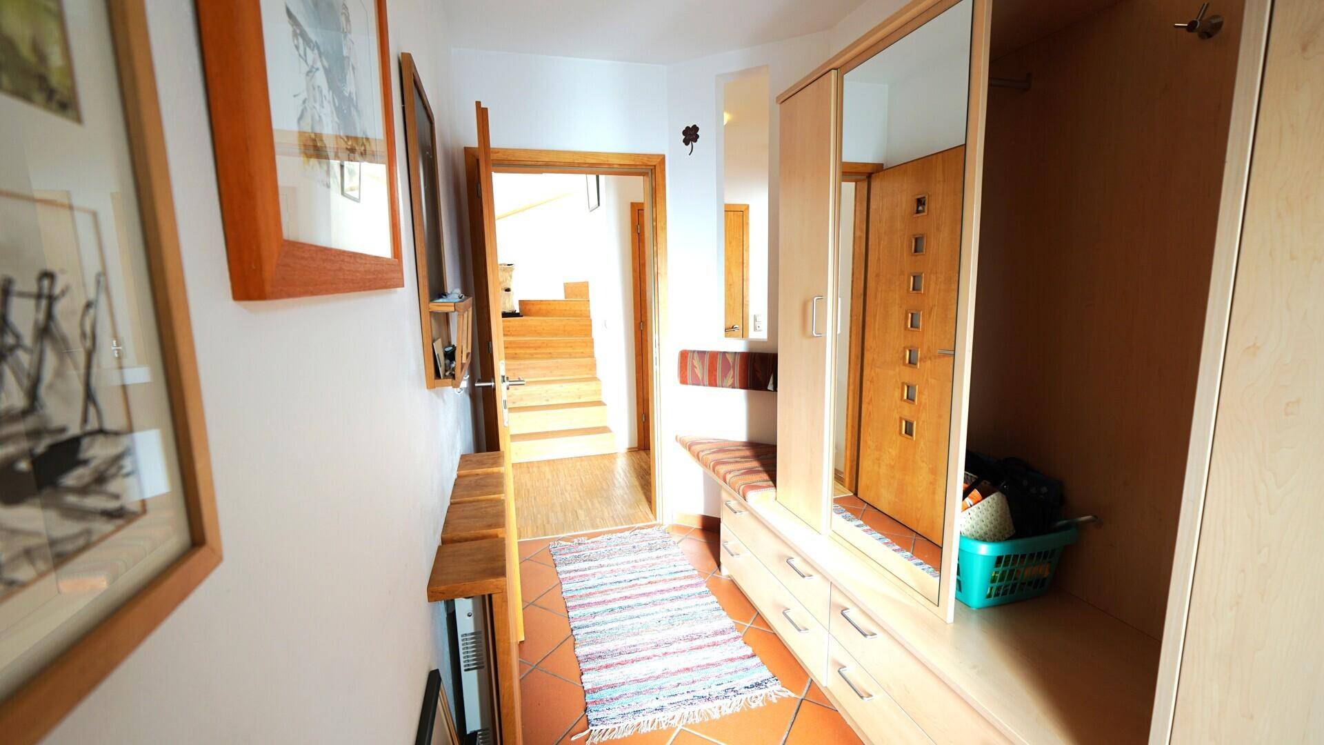 Heller Flur mit Einbauschränken, Garderobe und Blick auf die Holztreppe ins Obergeschoss.