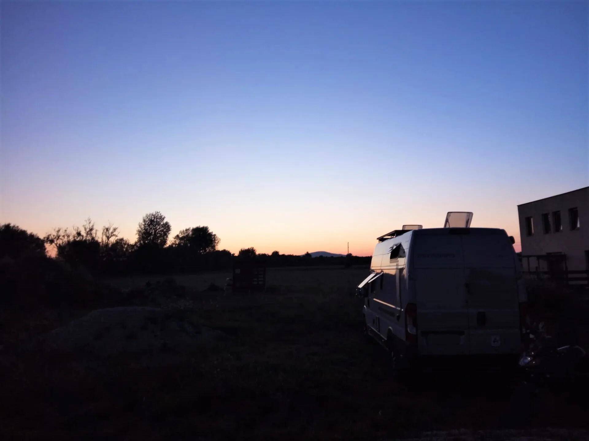 Abendstimmung auf dem Grundstück mit einem Wohnmobil und einem Gebäude im Hintergrund.