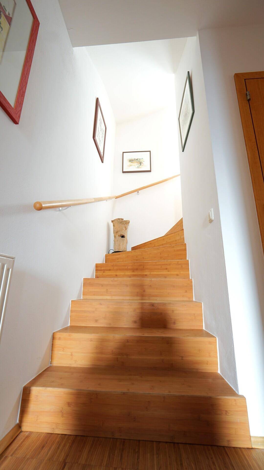 Holztreppe mit hellem Geländer führt in die oberen Stockwerke, gut beleuchtet.
